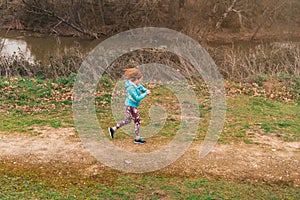 General shot of a sporty red-haired Caucasian female running while checking her surpluses outdoor