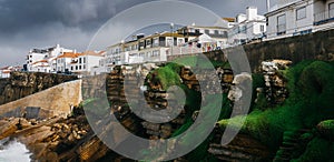 General view of Ericeira beach and houses and sea moss n cliffs under a cloudy winter sky, Portugal.