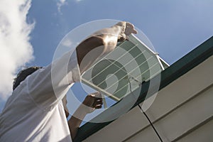 Generated iA man mounting a small 50 watt Polycrystalline solar panel on the eaves of a roof of a bungalow house