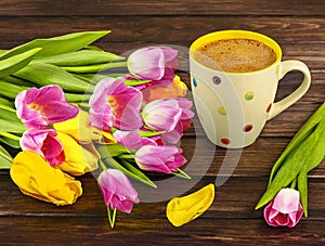 Spring bouquet of yellow and pink tulips and a white polka dot cup of coffee on a dark wooden background.ted image