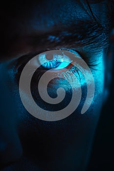 Glowing blue eye of a mysterious man. Serious expression. Evil man in the dark.