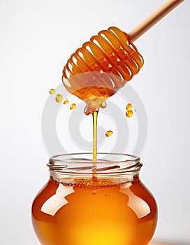 Honey dripping from a wooden honey dipper into a jar on white background