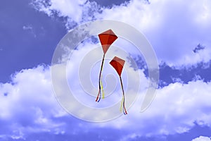 Two red kites flying against a blue sky with white clouds.