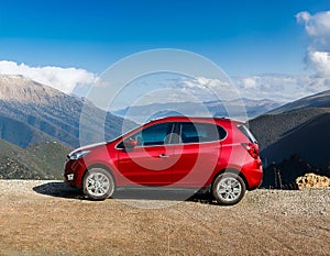 A new red car pulled over on the side of a remote mountain road