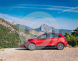 A new red car pulled over on the side of a remote mountain road