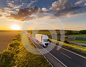 Truck with cargo driving on motorway at sunset with cloudy sky.