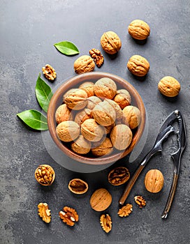 Fresh walnuts in bowl and nutcracker on gray table, flat lay.
