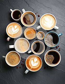 Cups with different types of coffee on dark grey table, flat lay
