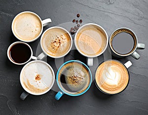 Cups with different types of coffee on dark grey table, flat lay
