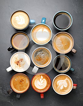 Cups with different types of coffee on dark grey table, flat lay