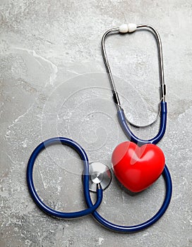 Stethoscope and red heart on grey stone table. Space for text