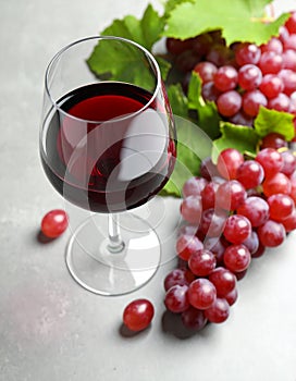 Fresh ripe grapes and a glass of wine on a gray table, close up.