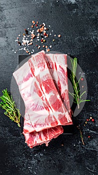 Raw ribs with rosemary and salt on black table, closeup
