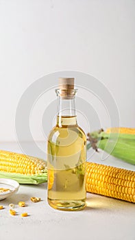 Bottle of corn oil and fresh cobs on table against light wall