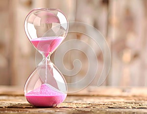 Hourglass with pink flowing sand on wooden table. Space for text