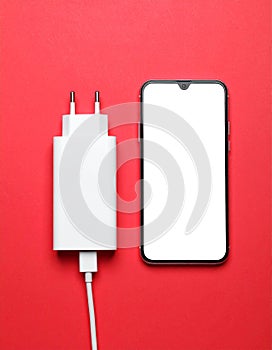 Smartphone and USB charger on red background, flat lay. Modern technology