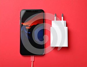 Smartphone and USB charger on red background, flat lay. Modern technology