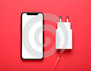 Smartphone and USB charger on red background, flat lay. Modern technology