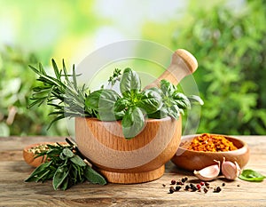 Different aromatic herbs, mortar with pestle and spices on wooden table, closeup