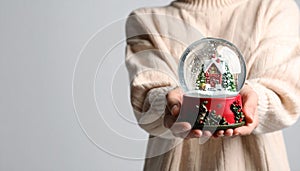 Woman holding decorative snow globe on grey background, closeup. Space for text