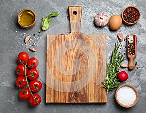 Cooking concept. Wooden cutting board and different products on grey textured table