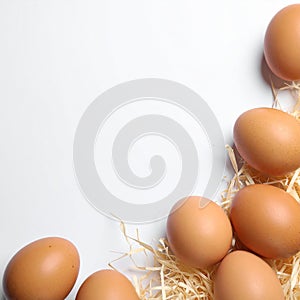 Raw chicken eggs and decorative straw on white table, flat lay. Space for text