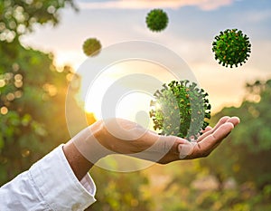 Human hand holding green virus model with sunlight and nature background