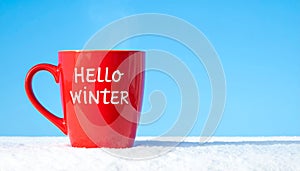 Red mug with words Hello winter on the blue background.