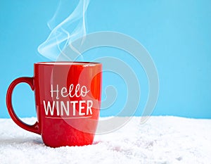 Red mug with words Hello winter on the blue background.
