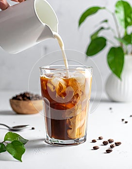 Pouring milk into a glass of iced coffee on a white table, closing