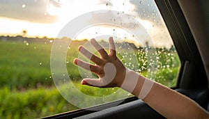 A close-up of a hand reaching out from a car window, with raindrops on the glass.