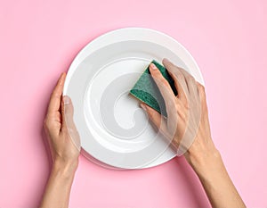 Woman washing dirty plate with sponge on pink background, top view