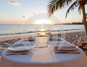 A table set for dinner on a sandy beach during sunset