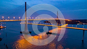 Illuminated Cable-Stayed Bridge at Dusk with Cargo Ship