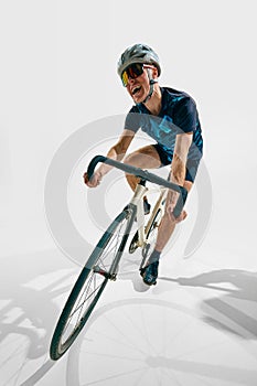 Full-length dynamic image of young man, professional cyclist in motion, training isolated on white background.