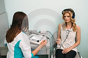 A healthcare professional administers a hearing test to a patient in a clinical setting using specialized audiometry equipment.