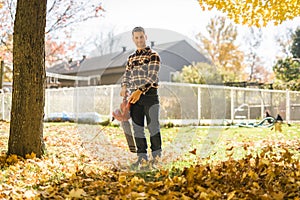 A Man cleaning fallen leaves using a leaf blower on the lawn.