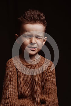 Portrait of frowning serious angry stylish white Caucasian child boy kid preschooler on a chair