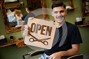 Smiling man coiffeur holding sign with open inscription in barbershop photo