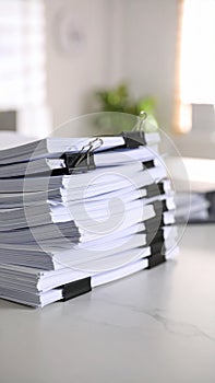 Stack of white paper documents bound with black binder clips on a white surface