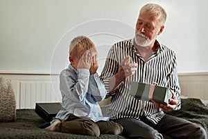 Generation. grandfather and grandson with gift box sitting on couch at home