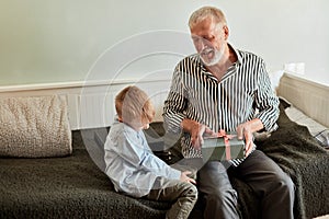 Generation. grandfather and grandson with gift box sitting on couch at home