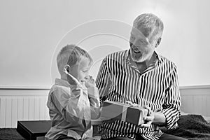 Generation. grandfather and grandson with gift box sitting on couch at home