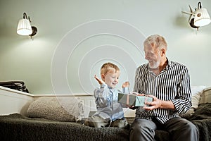 Generation. grandfather and grandson with gift box sitting on couch at home