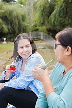 Generational Tradition: Latin Mother and Adult Daughter Share Yerba Mate on Blanket in Countryside Landscape