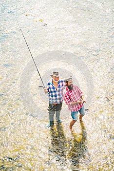 Generations ages: grandfather and father. Fishing in river. Young man and old mature man fly fishing. Father with son on