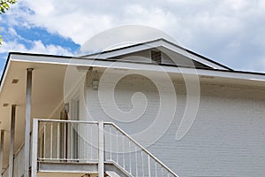 Generic brick apartment building painted white, second floor with metal railing and stairs, blue sky and white clouds behind