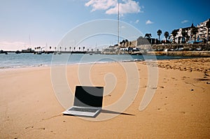 Generic notebook laptop on sunny deserted sandy beach background