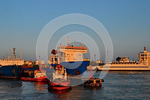 Generic view of industrial harbor with big white blue ships, red boats, vessels docked in harbor, warm orange sunset light