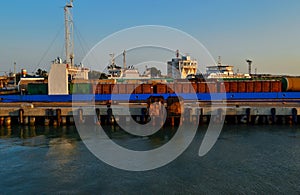 Generic view of industrial harbor, ships, barges with cargo, docked. Seascape in sunset light. Blue sky gradient
